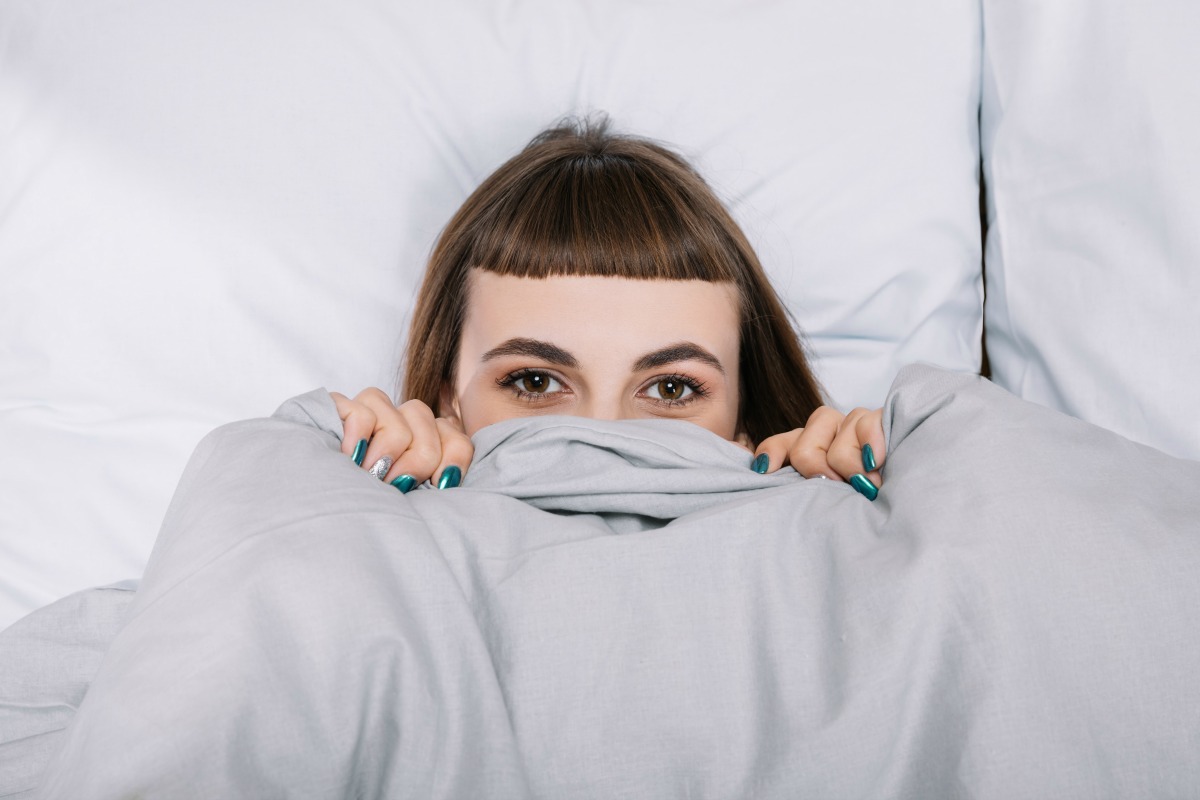 Woman lying in a bed with a weighted blanket pulled up to her face.