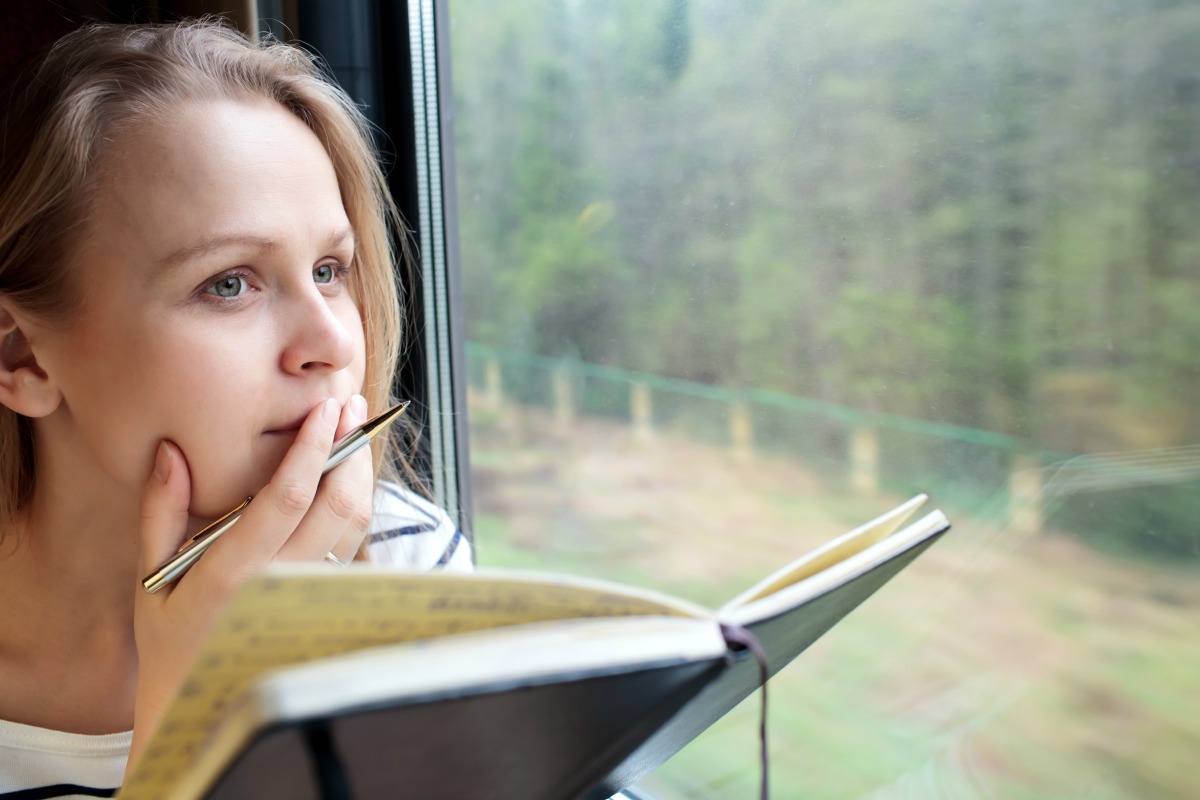 Woman staring out of a window while writing in a journal
